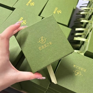 Detalle de caja de regalo verde oscuro para joyas con logo dorado y cinta de seda