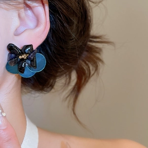 Close-up of a floral earring with black faux stone, blue translucent petals, and gold beads