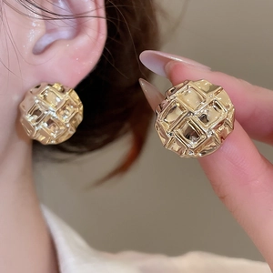 Macro detail of round golden quilted texture earrings with embossed lattice pattern