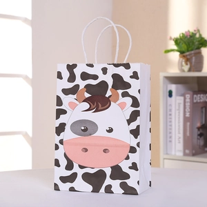 Close-up of a cartoon cow print party gift bag with white braided handles on a table