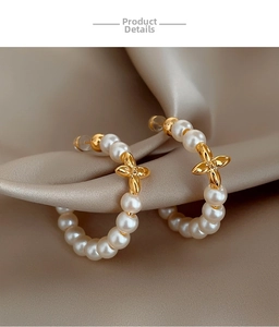 Macro shot of pearl hoop earrings with gold floral motifs on champagne silk fabric