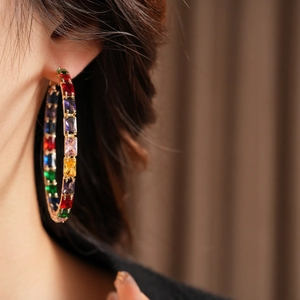 Close-up of large gold hoop earrings with multi-color rectangular zircon stones