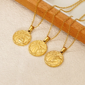 Close-up of three gold zodiac necklaces featuring embossed round pendants on beige fabric