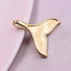 Macro shot of 18k gold plated fishtail pendant on a pink plate with soft shadows