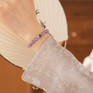 Detail of amethyst beaded bracelet with hollow silver floral charm on a female wrist