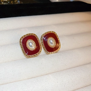 Macro detail of red enamel square earrings with oval pearl and golden embossed border