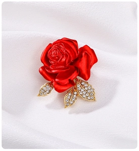 Macro shot of red rose brooch with golden leaves and crystals on white cloth