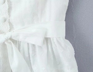 Détail du tissu blanc texturé à pois avec ceinture nouée et boutons recouverts