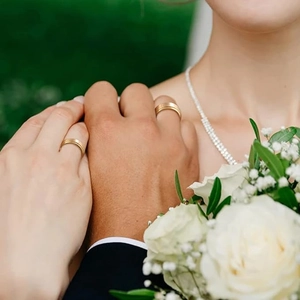 Close-up of brushed gold wedding bands worn by a couple with white roses in the background