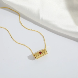 Detail of gold lucky pendant with red heart gemstone and happy engraving on white silk