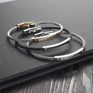 Detail of silver and black steel cable woven bracelets layered on a dark notebook