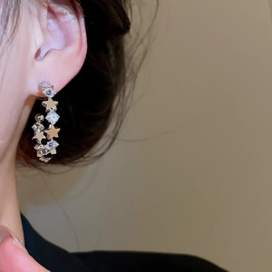 Detailed view of silver C-shape hoop earrings with sparkling zircon stars on ear