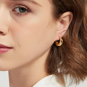 Close-up of thick gold-plated geometric hoop earrings worn by a female model