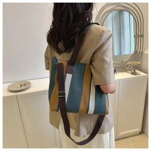 Vertical striped canvas tote bag in green and yellow worn by a model in a minimalist room