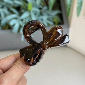 Detail of tortoise shell resin bow hair claw clip held by hand in amber finish