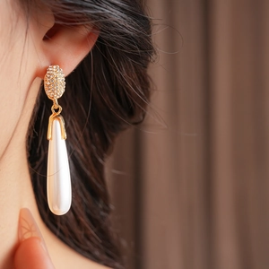 Close-up of elegant gold drop earrings with white pearls and sparkling rhinestones