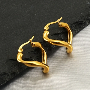 Detailed close-up of golden twisted heart-shaped earrings on textured slate and silk