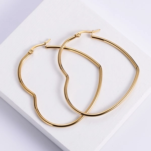 Polished gold heart hoop earrings in minimalist style on white textured stone background
