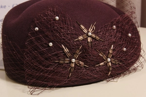 Detailed close-up of wool beret with burgundy veil and hand-beaded pearl star design