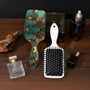 Elegant marble print paddle hairbrush set on dark wood background with cosmetic props