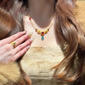 Macro detail of ethnic gold necklace with red gems and blue resin teardrop pendants