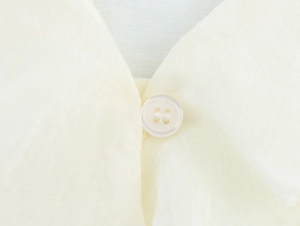 Macro view of creamy white four-hole button on soft light beige fabric texture