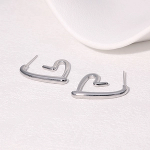 Minimalist silver heart shaped stainless steel stud earrings on a textured white background