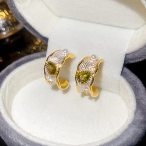 Detailed close-up of golden C-shaped pearl earrings with green zircon in a jewelry box