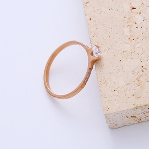 Minimalist rose gold titanium ring with a central zircon set on beige stone background