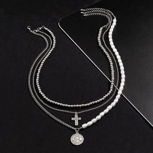 Layered cross and pearl necklace with silver bead chain on black textured background