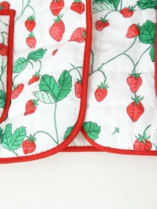 Detail view of strawberry print quilted fabric with red piping on padded jacket