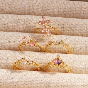 Gros plan détaillé de cinq bagues dorées avec zircons roses et violets dans un écrin à bijoux
