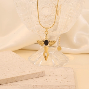 Golden cross necklace with angel wings and black oval gemstone on a glass cup