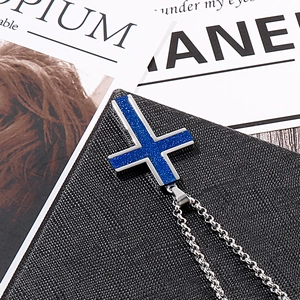 Detailed view of silver cross necklace with blue glitter inlay on a black surface