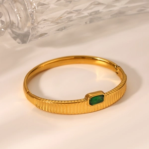 Detailed macro of gold-plated ribbed stainless steel bangle with green rectangular zircon