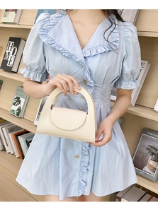 Detail of a beige compact leather handbag featuring a round handle and chic flap closure