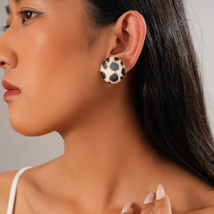 Close-up of model wearing round earrings with cow print pattern and silver needles