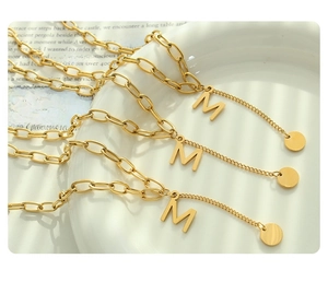 Close-up of golden M letter pendant with layered thick and fine chain jewelry strands