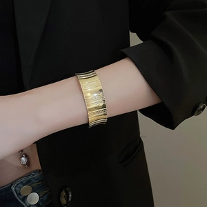 Detail of wide gold textured cuff bracelet worn on model with black suit jacket