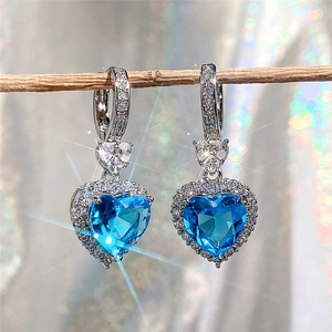 Macro shot of heart-shaped blue topaz earrings with sparkling halo on branch
