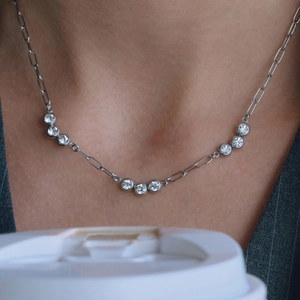 Close-up of a silver paperclip chain necklace with nine round zircon stones on a female model