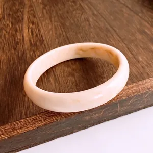 Bracelet jonc minimaliste en résine avec motif marbre crème sur plateau en bois vintage