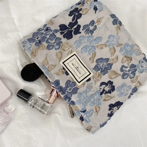 Close-up of blue floral embossed makeup bag with golden zipper and logo patch