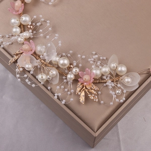 Detailaufnahme von goldenem Haarband mit Perlen und rosa Kristallblüten auf Seide