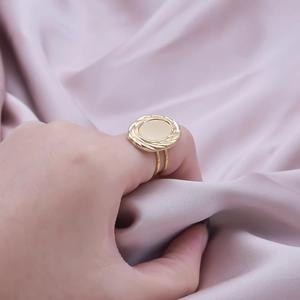 Close-up of golden oval ring with twisted rope border worn on a finger against silk