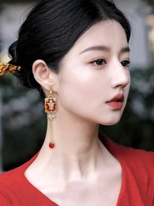 Close-up of red enamel flower earrings with gold tassels and pearls on model