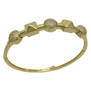 Golden bangle with pyramid studs and pavé zircon spheres on a minimalist white surface