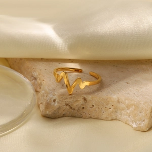 Detail of adjustable 18K gold plated heart rate ring on beige stone and silk background