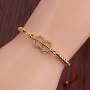 Close-up of golden heart and arrow zircon bracelet with adjustable red cord on model