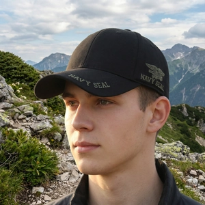 Men's black Navy Seal baseball cap with green embroidery against a mountain background